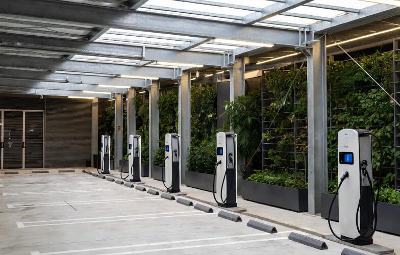 Luftfoto og indendørsbillede af et stilrent, moderne parkeringshus med flere hvide og sorte elbil-ladestationer placeret ved parkeringsbåsene.